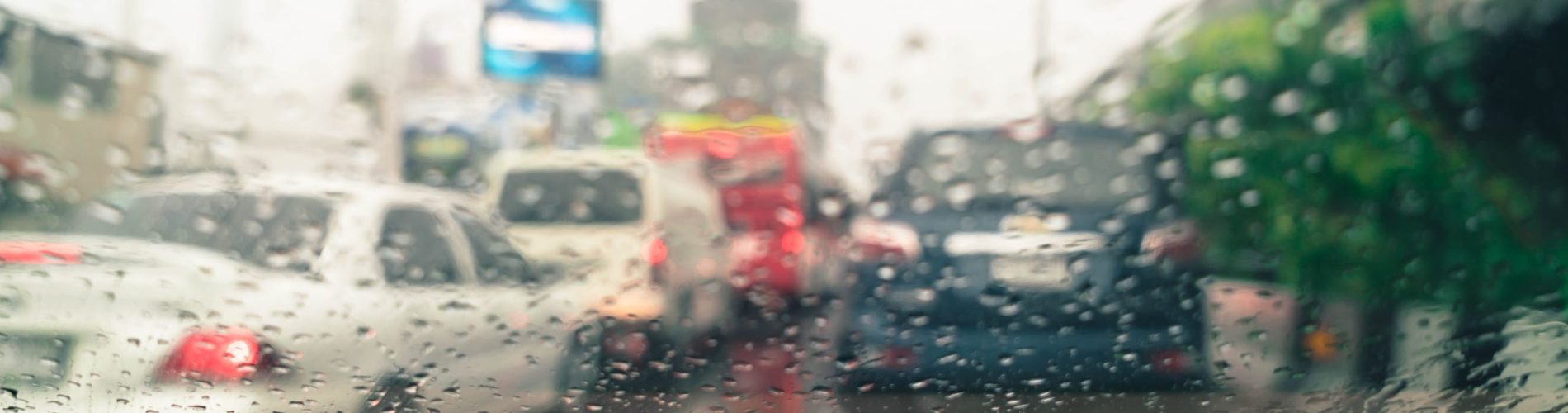 Gotas de chuva no vidro do carro durante condução, reduzindo a visibilidade e destacando riscos na direção e na frenagem em pista molhada.