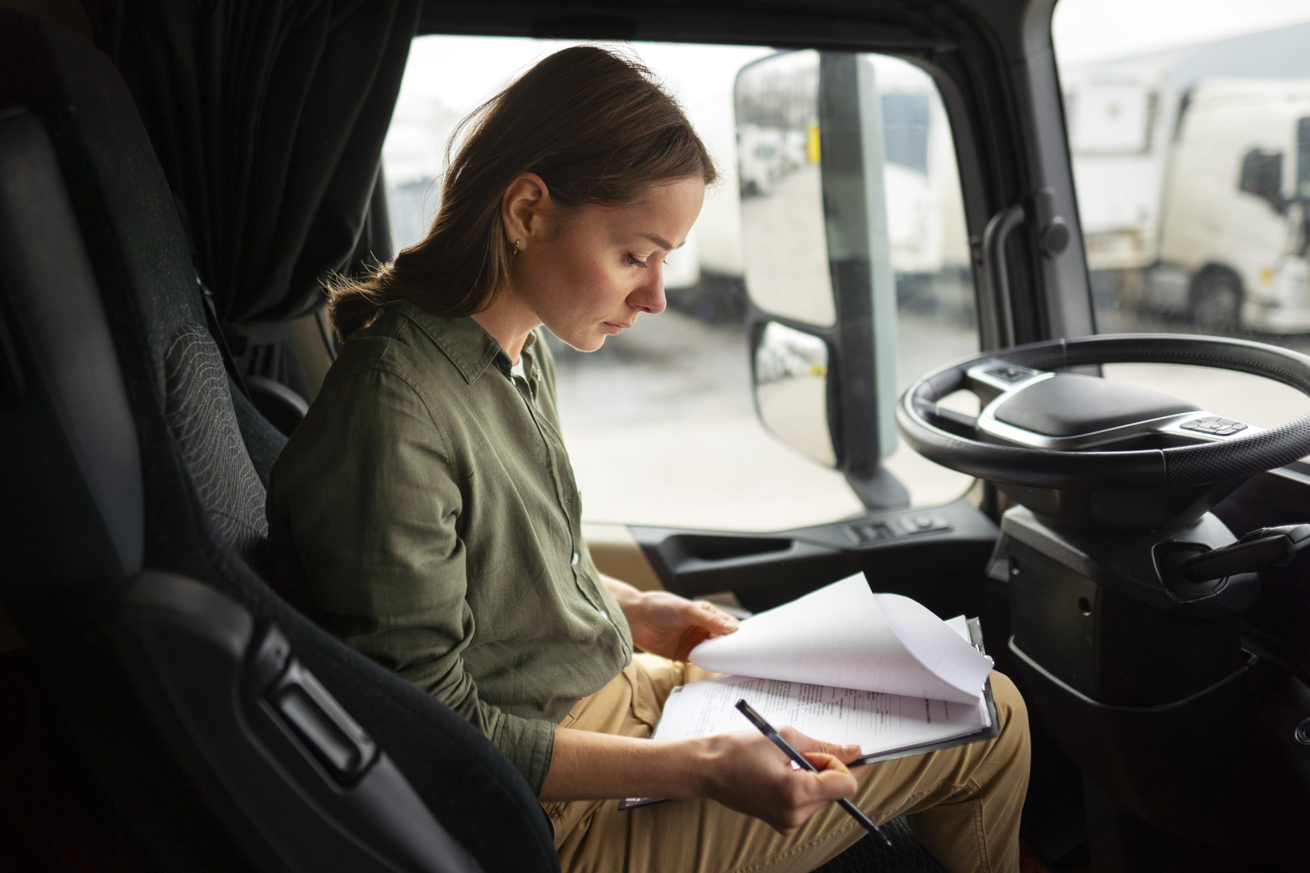 Gestora de frotas dentro da cabine do caminhão olhando documentos enquanto trabalha no volante durante a jornada de transporte.