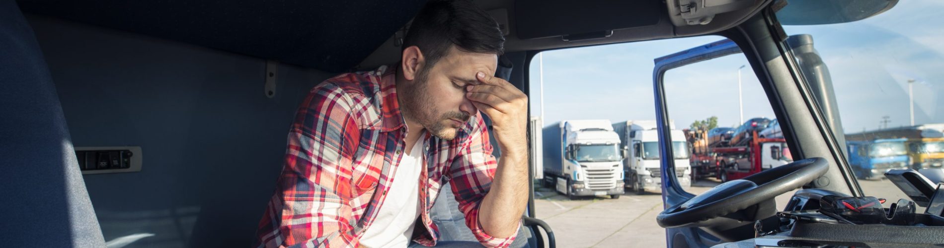 Motorista de caminhão sentado na cabine com expressão preocupada, representando preocupação com multa de trânsito e pontos na CNH durante a operação de transporte.