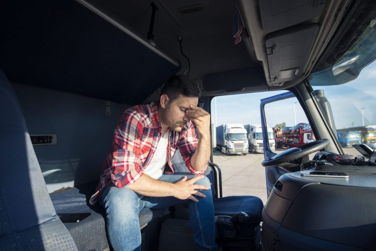 Motorista de caminhão sentado na cabine com expressão preocupada, representando preocupação com multa de trânsito e pontos na CNH durante a operação de transporte.