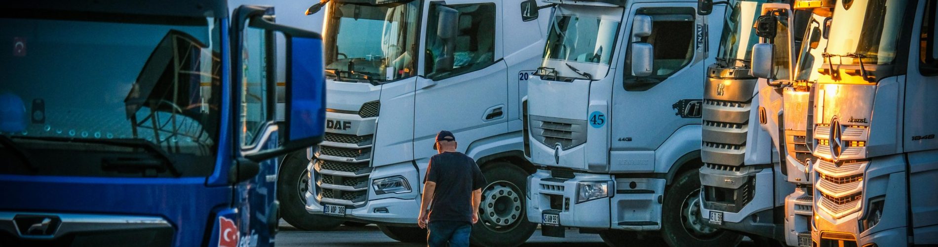 Frota de veículos pesados parada em centro de distribuição ao final do dia, representando a logística e o tempo de vida útil dos ativos.